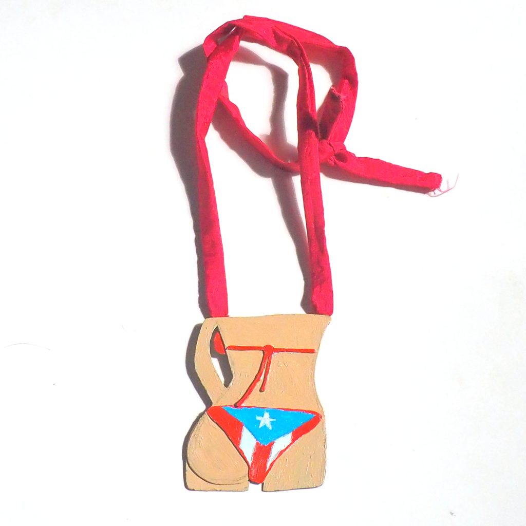 A necklace. On a red hand sewn silk ribbon is a metal pendant of a woman's torsopainted